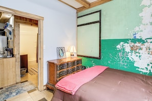 Un dormitorio con cama, cómoda y pared verde con pintura descascarada.