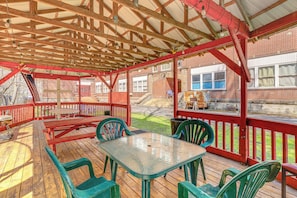 A covered outdoor deck with picnic tables and chairs, a wooden ceiling, and a brick building in the background. - Warrior Trail Access! Converted Schoolhouse Suite (Gary)