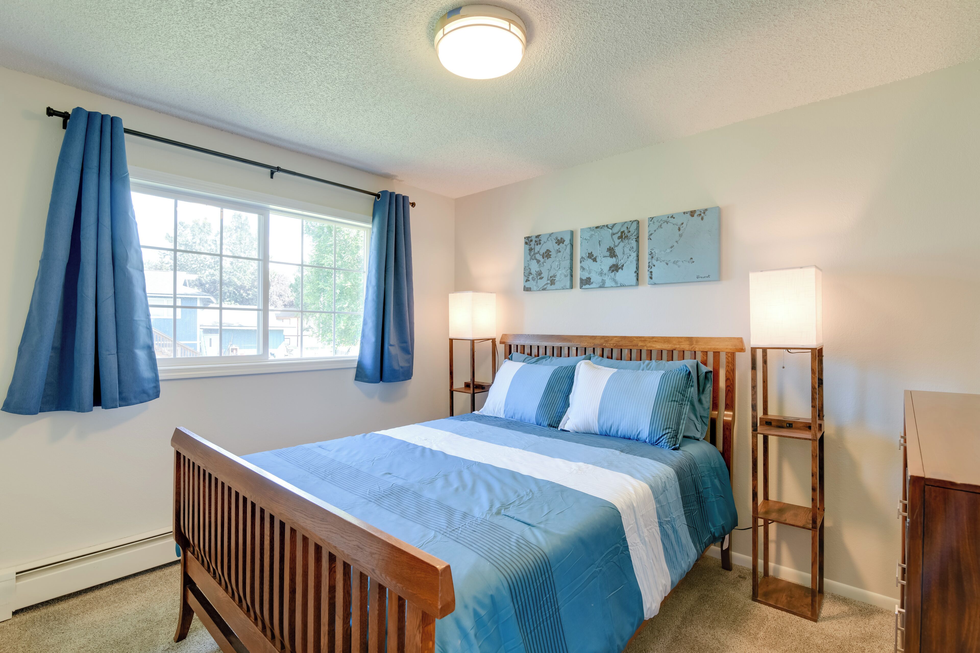A bedroom with a wooden bed, blue curtains, a window, and two bedside lamps.