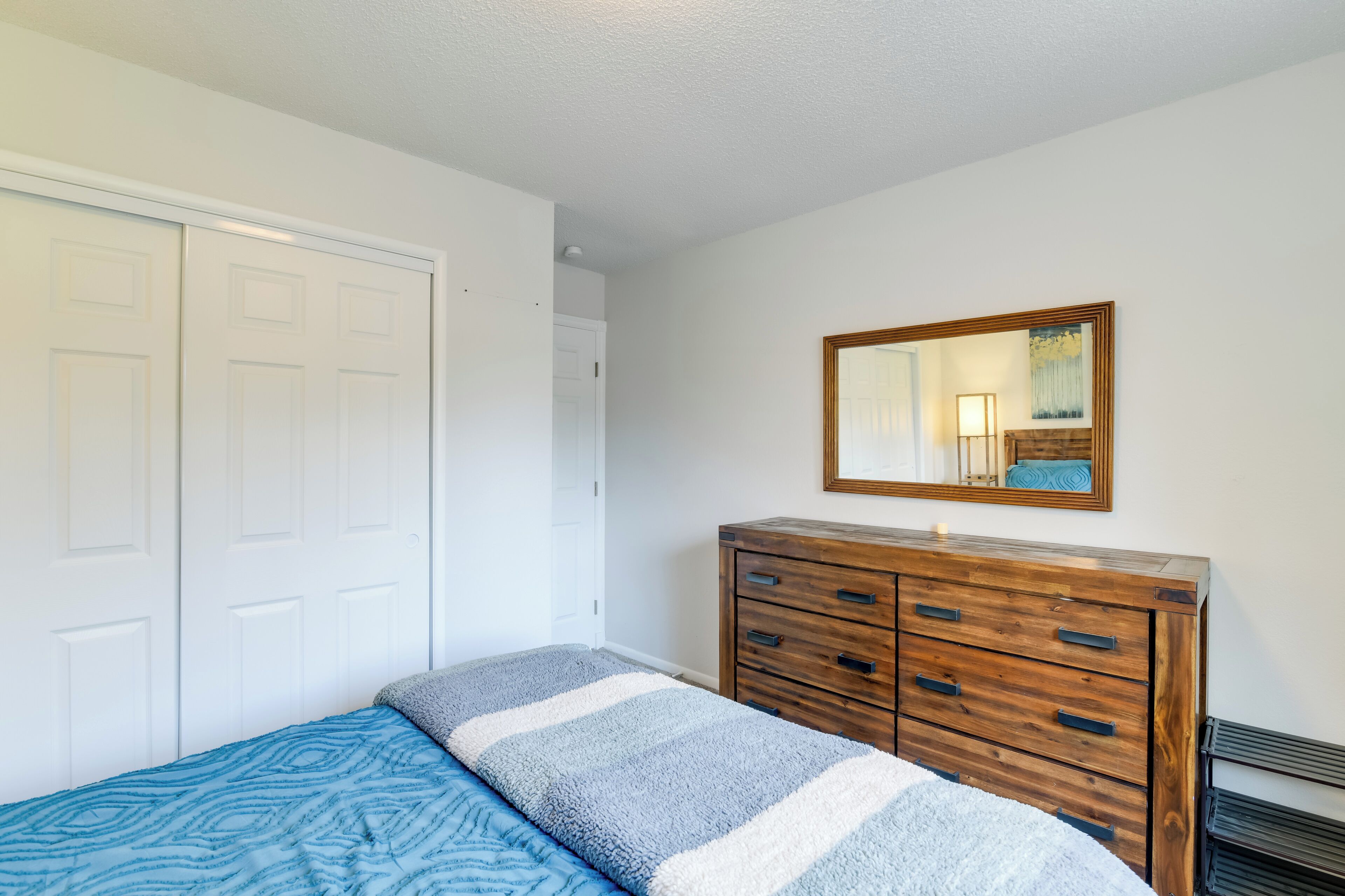 Une chambre à coucher avec un lit, une commode, un miroir et une porte.