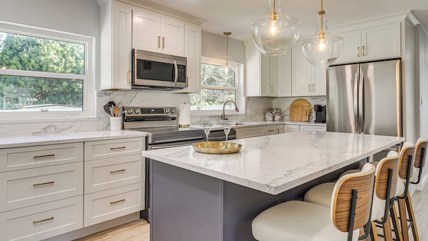 A modern kitchen with white cabinets, stainless steel appliances, a marble island, and bar stools. - Beach-hop, Bike & Bbq! Clearwater Home w/ Yard (Clearwater)