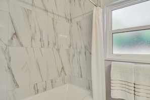 A bathroom with marble walls, a bathtub, a window with frosted glass, and a towel rack with towels.