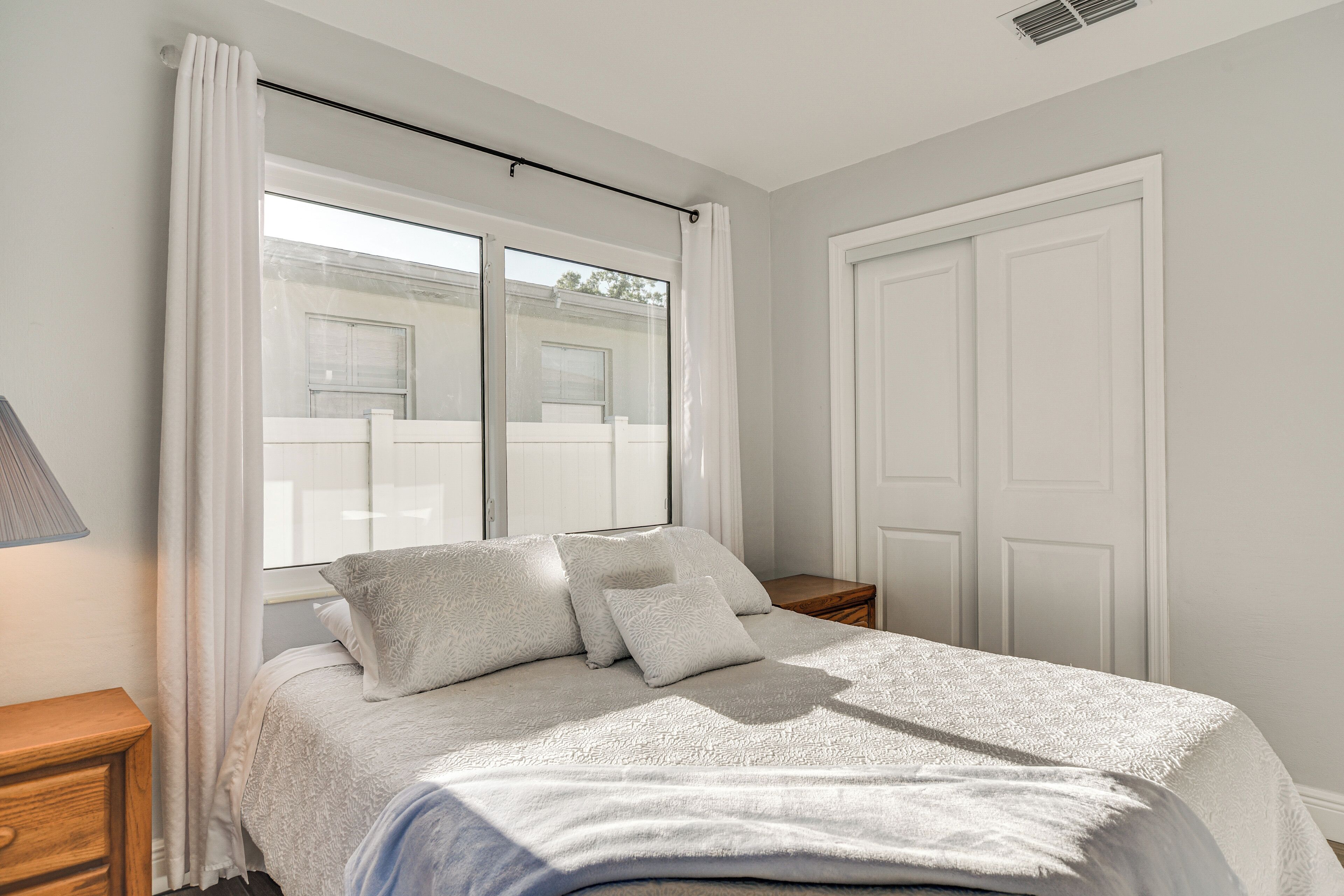A bedroom with a bed, a nightstand, a lamp, and a window with curtains.
