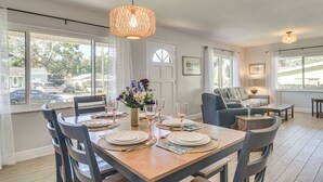 A dining area with a wooden table set for six, six chairs, a vase of flowers, and a hanging light fixture. - Beach-hop, Bike & Bbq! Clearwater Home w/ Yard (Clearwater)