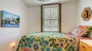 Een slaapkamer met een bed, een raam met zonwering, een hoed aan de muur en een schilderij.