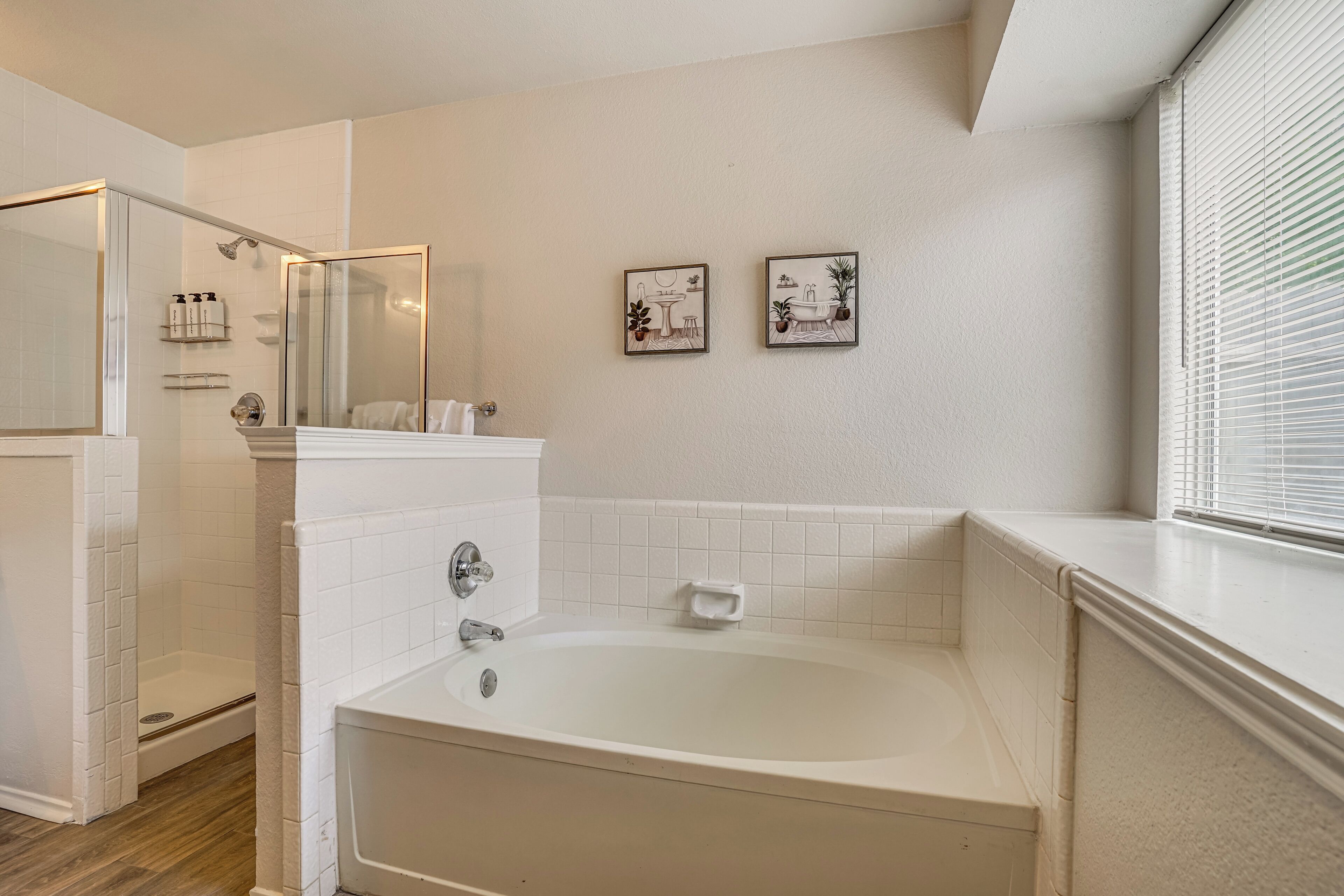A modern bathroom with a bathtub, a glass-enclosed shower, and two framed pictures on the wall.
