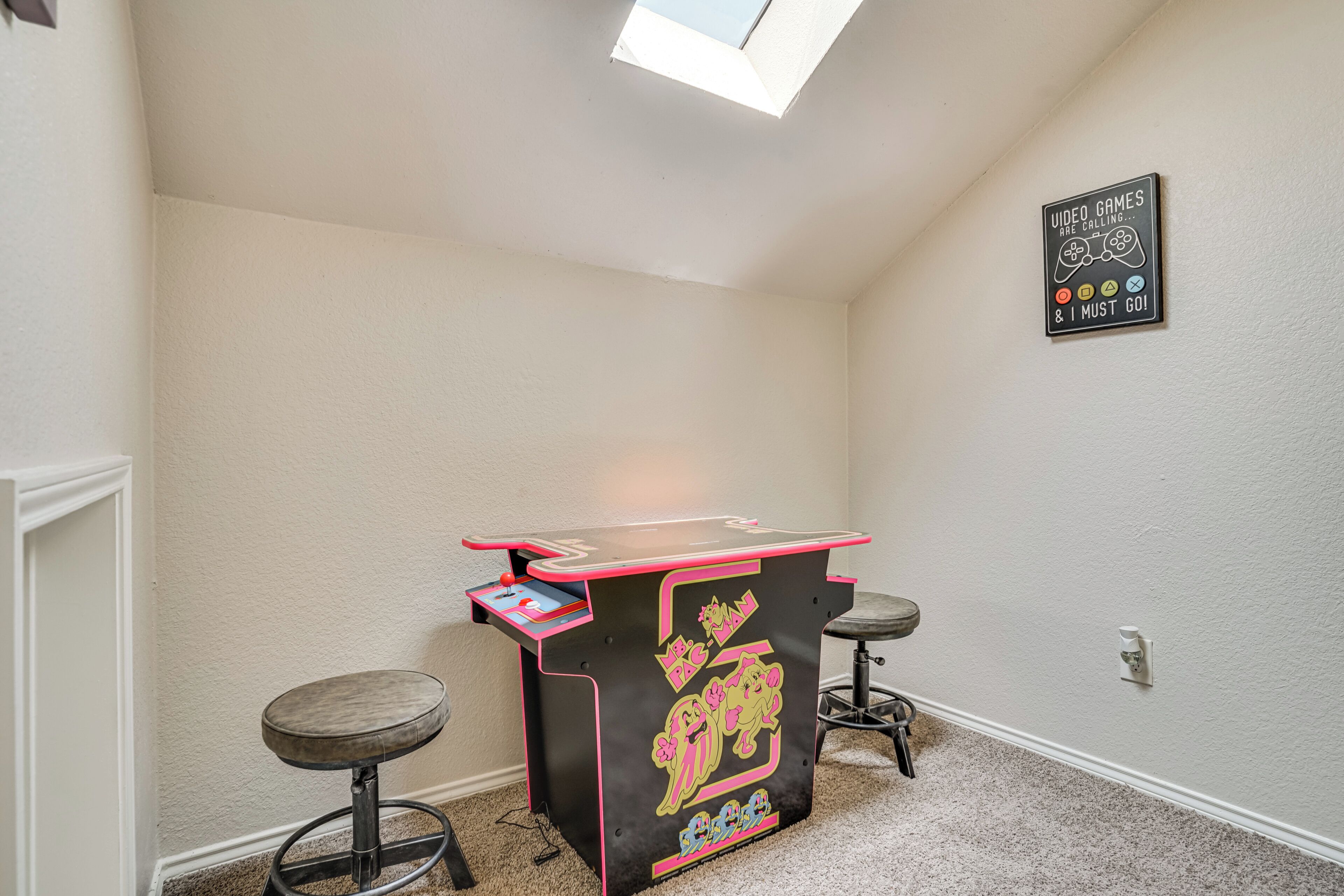 A small room with a ceiling light, a wall-mounted sign, a table with chairs, and a carpeted floor.