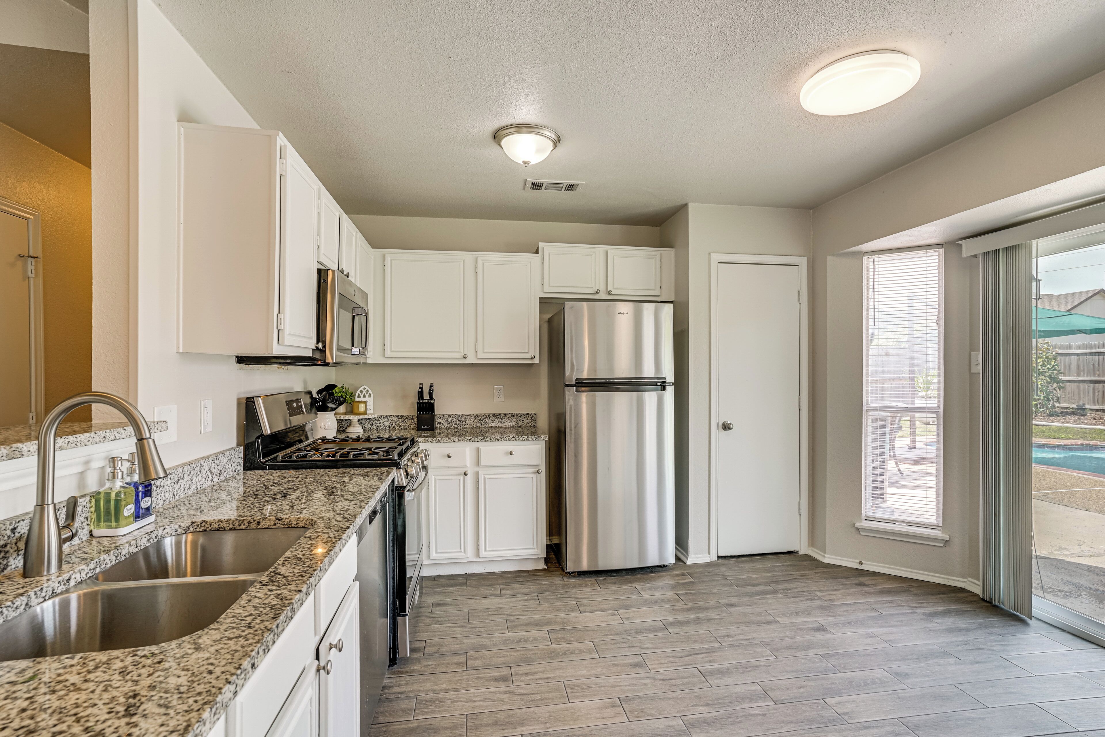 A kitchen with white cabinets, stainless steel appliances, granite countertops, and a view to the outside.