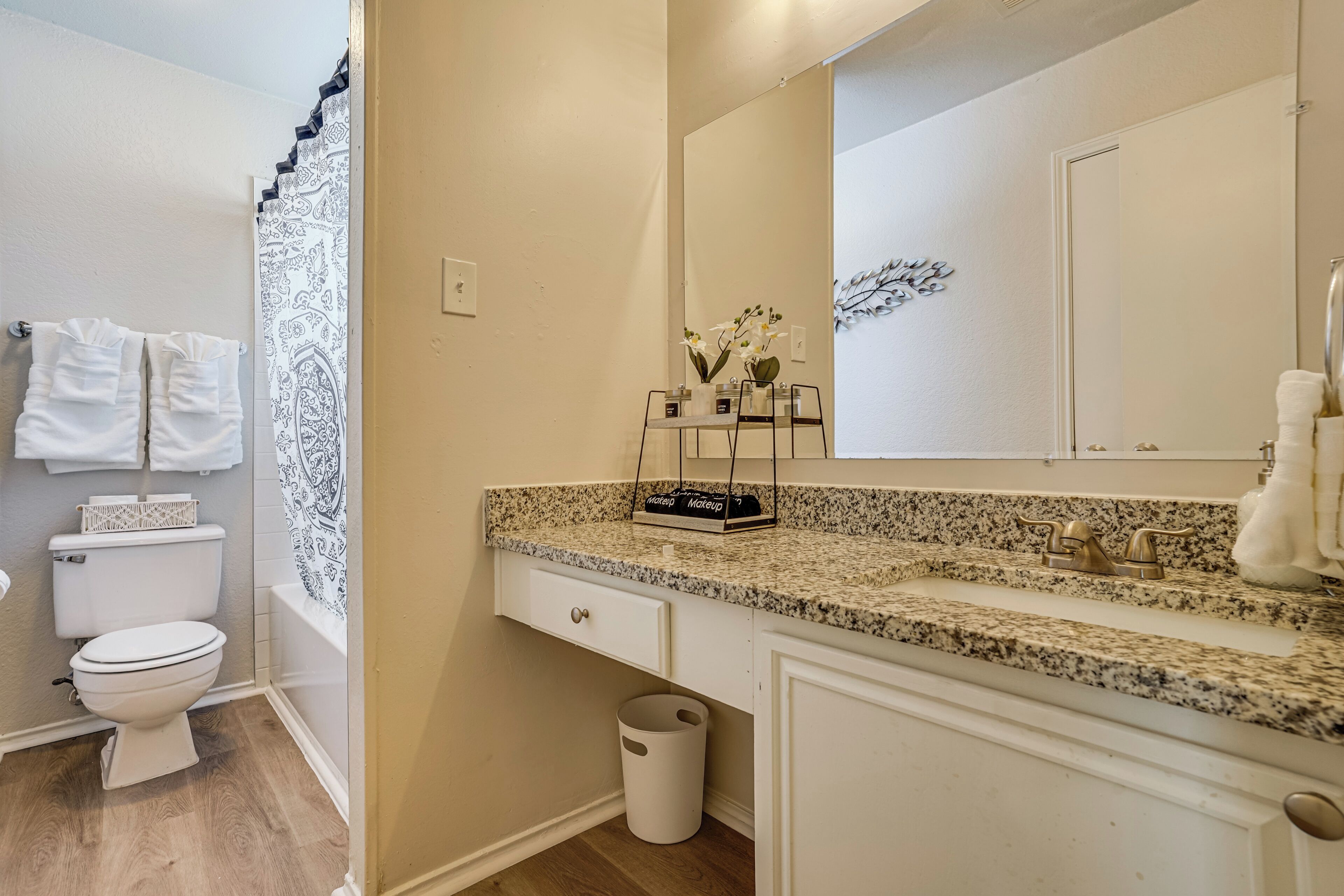A bathroom with a toilet, sink, mirror, and a trash can.
