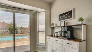 Una cocina con cafetera, una ventana con persianas y vista a un patio trasero con piscina.