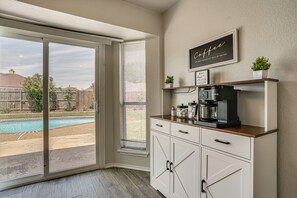 Eine Küche mit Kaffeemaschine, einem Fenster mit Jalousien und Blick auf einen Hinterhof mit Schwimmbad.