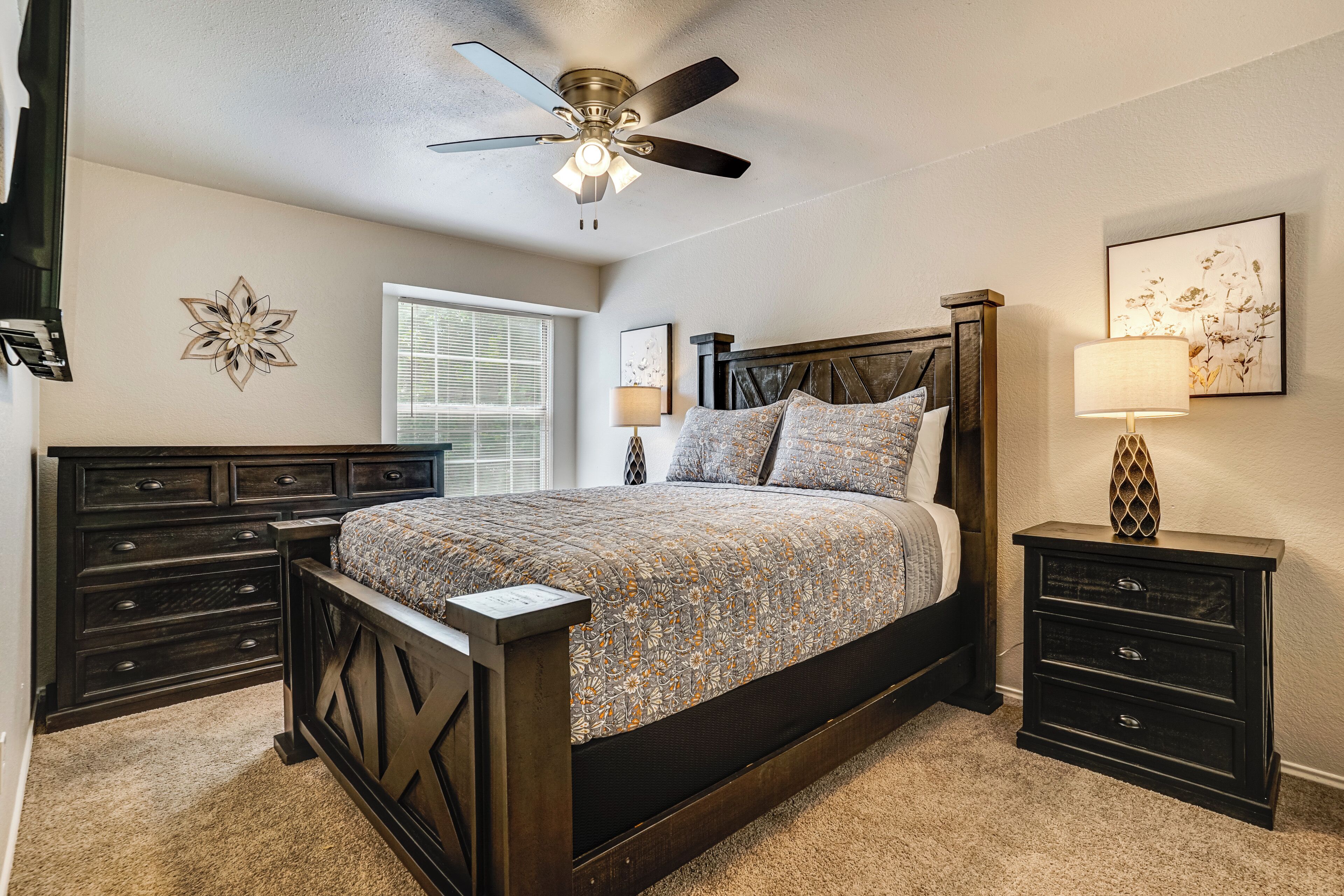 A bedroom with a bed, a nightstand, a ceiling fan, and a window.