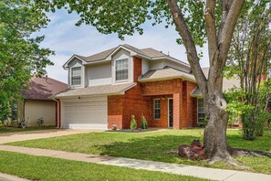 Ein zweistöckiges Haus mit Garage, einer Ziegel-Fassade und einem großen Baum im Vorgarten.
