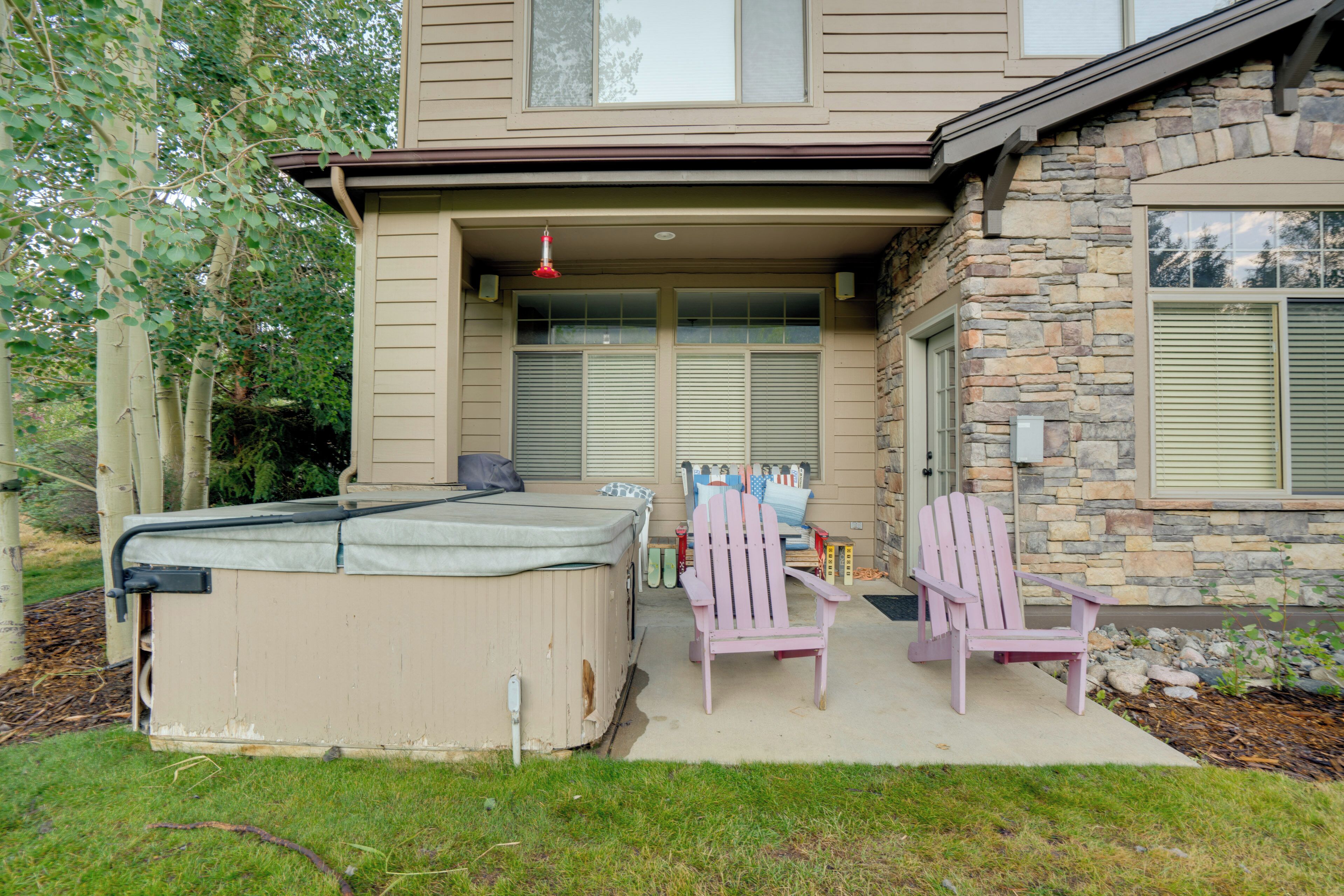 A house with a patio area featuring a hot tub, two Adirondack chairs, and a covered seating area.