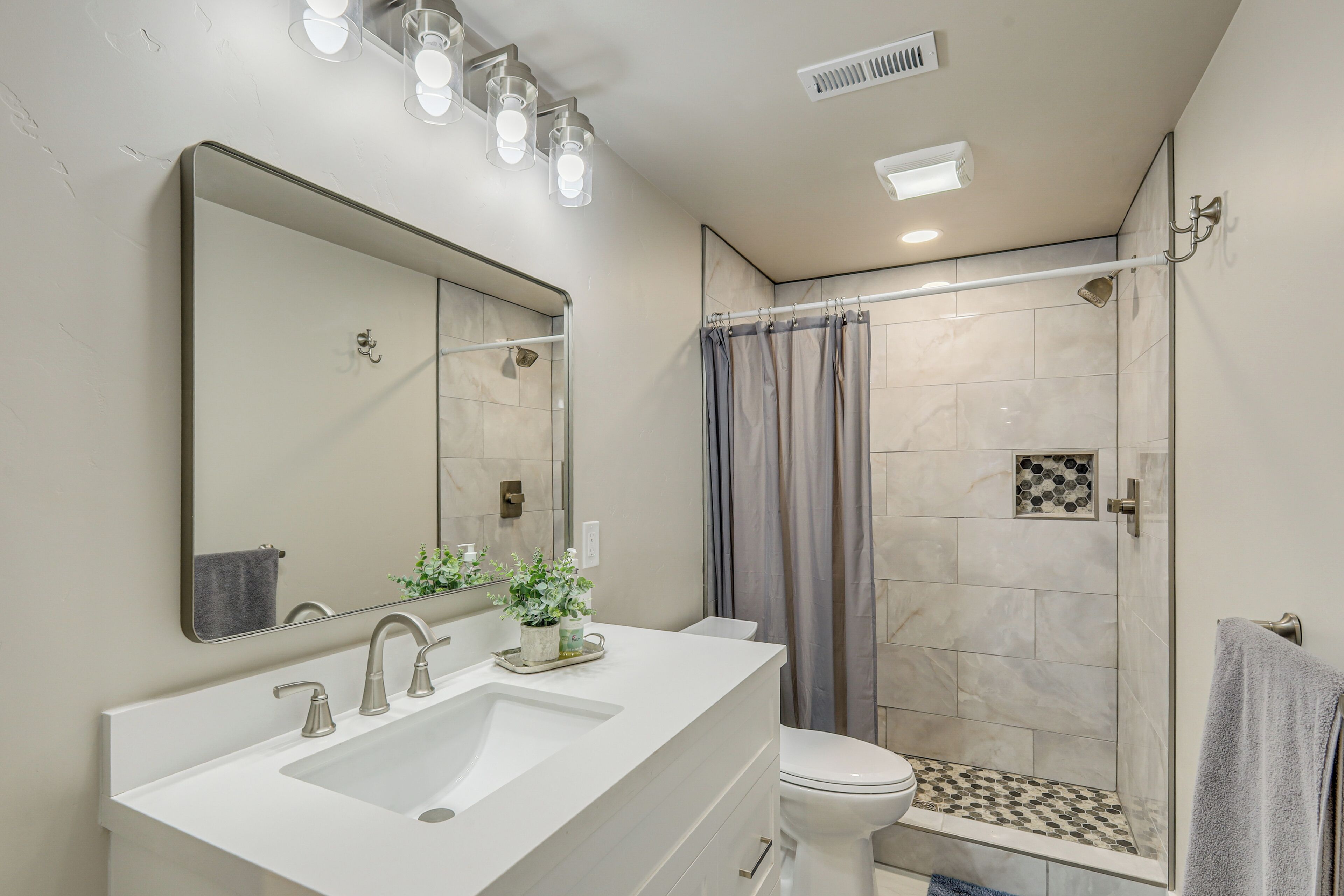 Une salle de bain équipée d’un lavabo, d’un miroir, de toilettes et d’une zone douche.