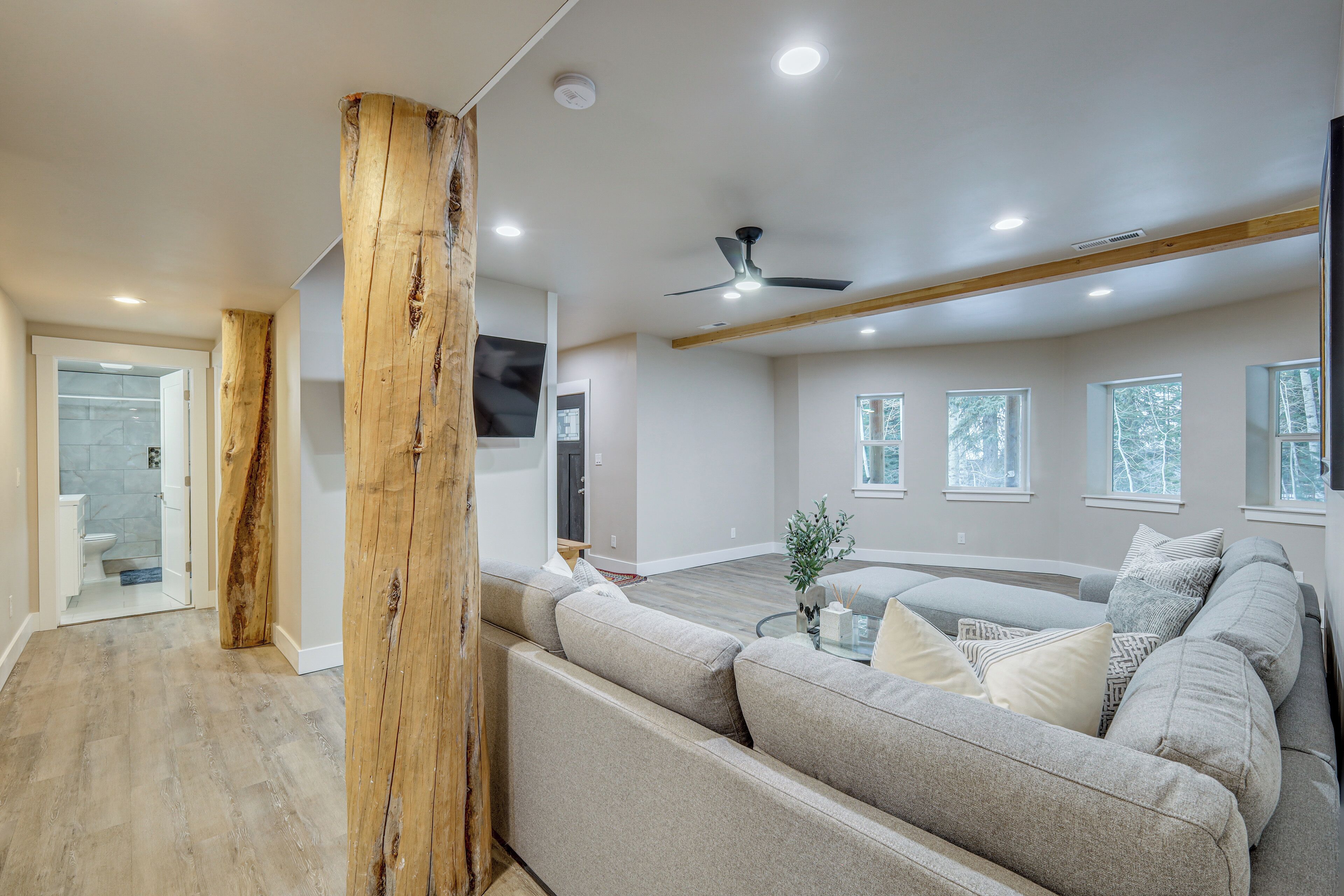 A spacious living area with a large sectional sofa, wooden beams, and a ceiling fan.