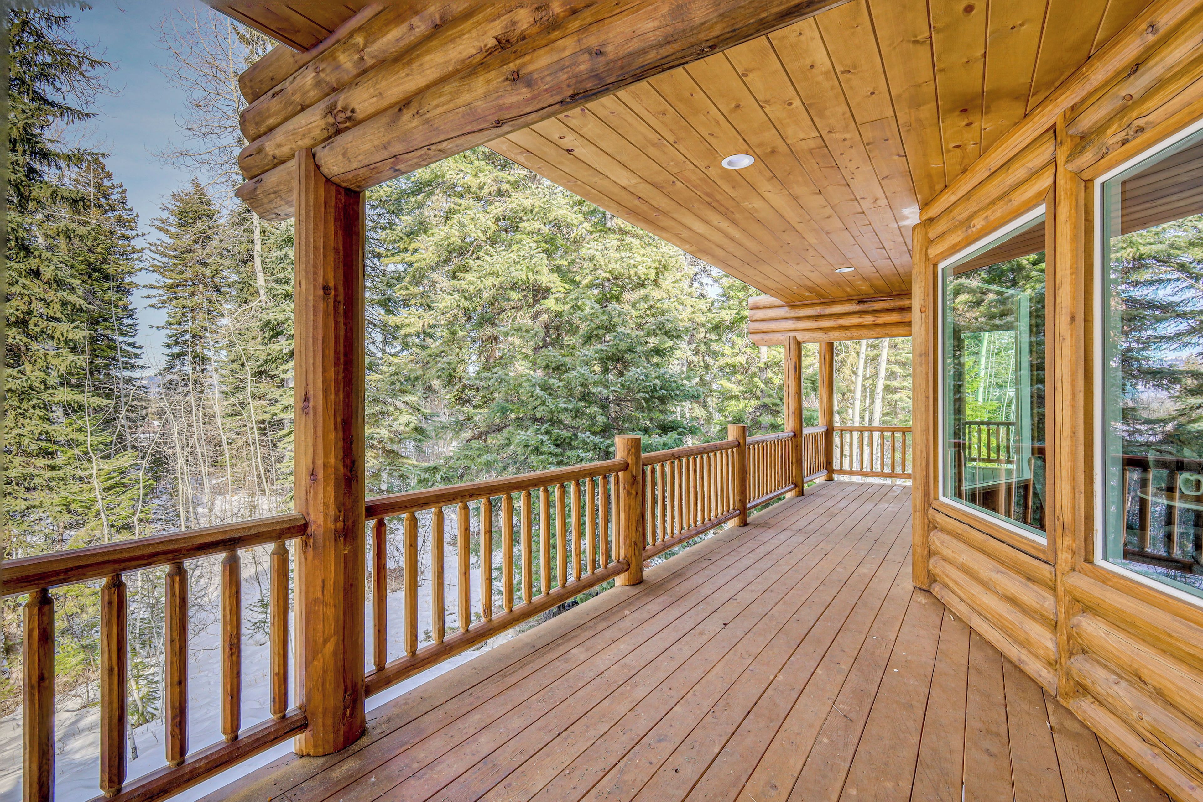 A wooden deck with a railing, large windows, and a view of a forest.