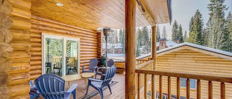 A wooden cabin with a deck, outdoor seating, and a view of trees.