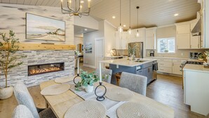 A modern kitchen with a central island, a dining area with a fireplace, and a view of the living room. - Luxury Mccall Lodge: Hike, Ski, Golf & More! (McCall)