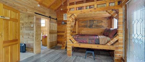A cozy log cabin interior with a loft bed, wooden walls, and a small kitchenette.