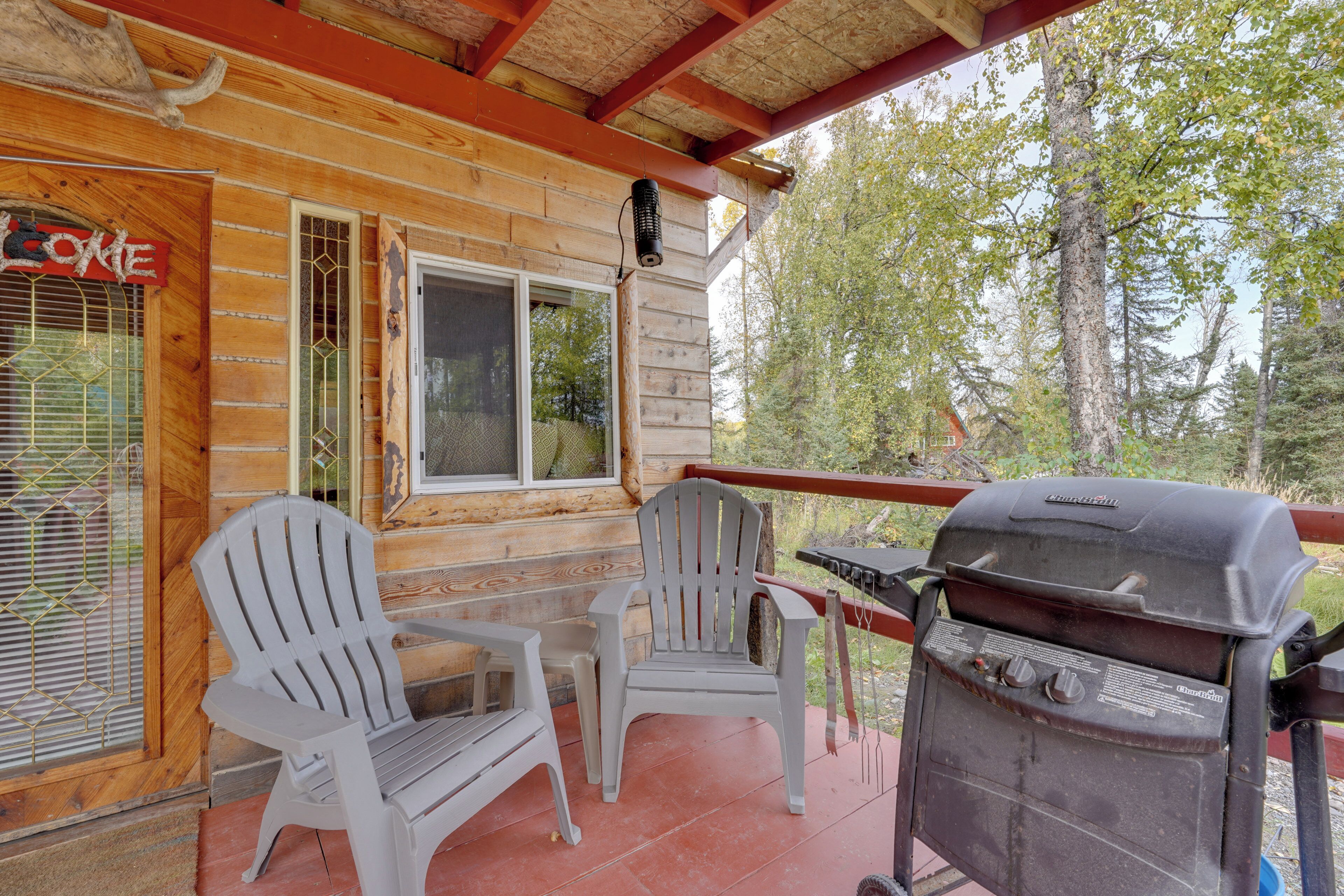 A wooden cabin with a porch, two Adirondack chairs, a grill, and a Coca-Cola sign.