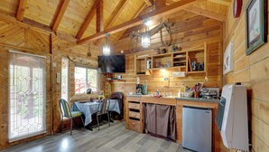 Interior de una cabaña de madera con comedor, cocina y un televisor en la pared.
