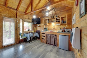 Ein Holzblockhaus-Interieur mit Essbereich, Küche und einem an der Wand montierten Fernseher.