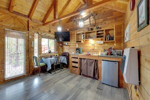 Interior de una cabaña de madera con comedor, cocina y un televisor en la pared.