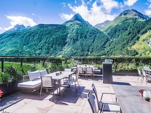Eine Terrasse mit Sitzgelegenheiten, Blick auf Berge und einen klaren Himmel.