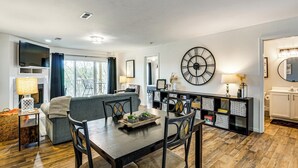 A modern living room with a dining table, chairs, a sofa, a TV, and a large wall clock. - Beach, Boat Slip, Views! Lake of the Ozarks Condo (Osage Beach)