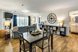 Ein modernes Wohnzimmer mit Esstisch, Stühlen, einer Couch, einem Fernseher und einer großen Wanduhr.