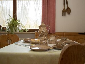Een eettafel gedekt met keramiek servies, een potplant en houten bestek aan de muur.