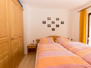 Een slaapkamer met een bed, nachtkastje, kledingkast en een muur met ingelijste foto's.