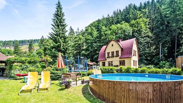 Un jardin avec une piscine en bois, une maison et, au loin, une colline boisée.