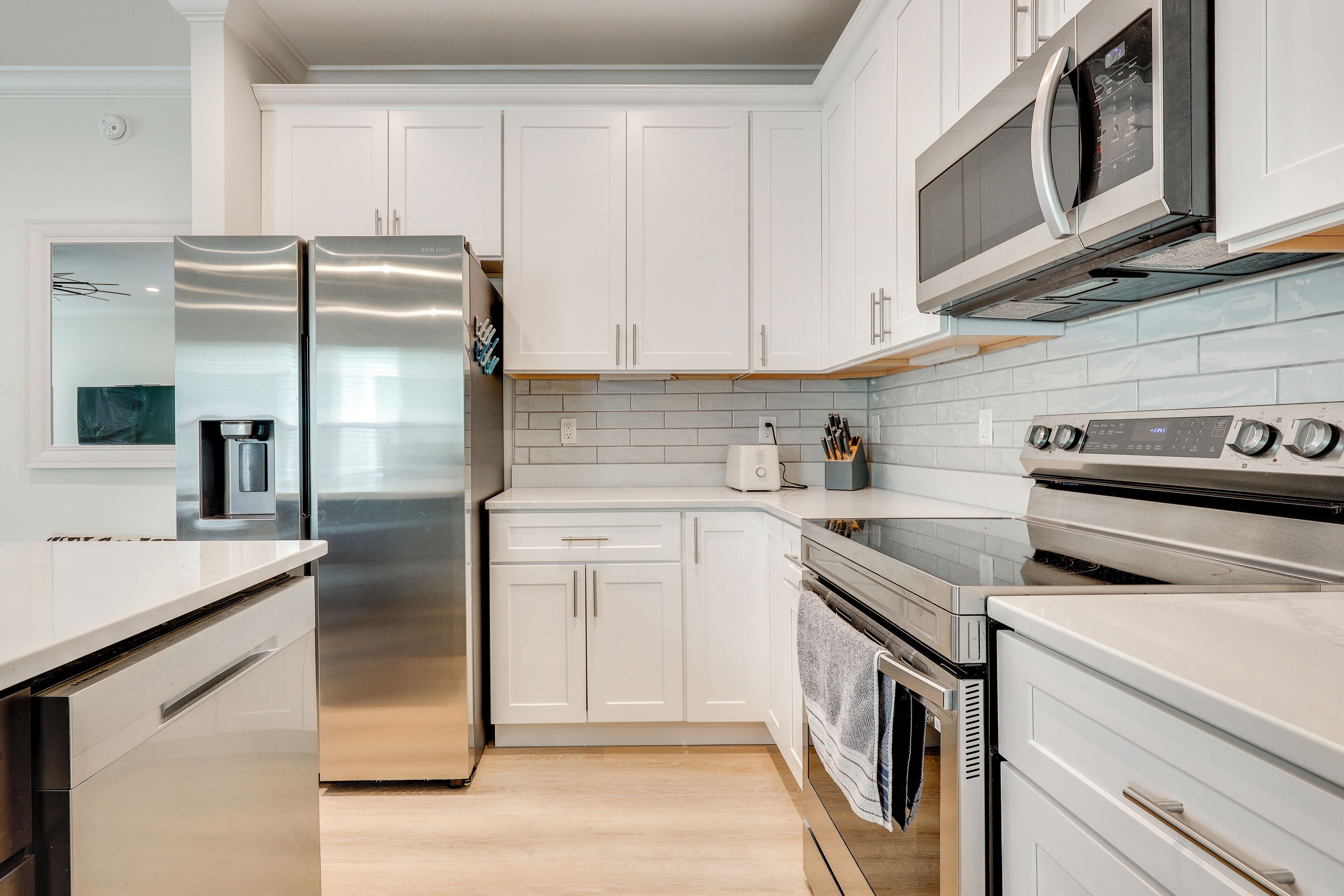 A modern kitchen with stainless steel appliances, white cabinetry, and a tiled backsplash.