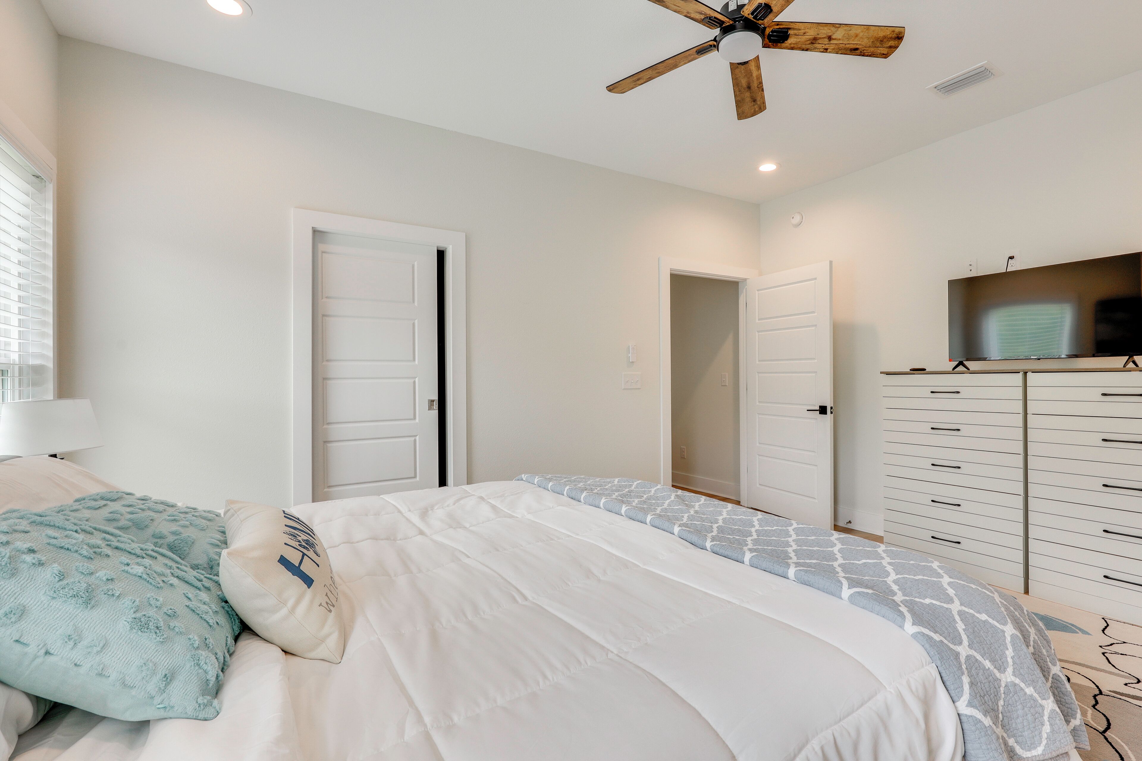 A bedroom with a bed, a ceiling fan, a TV on a stand, and a dresser.