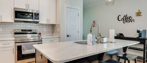 A modern kitchen with white cabinets, stainless steel appliances, a large island with stools, and a 'Coffee Bar' sign.