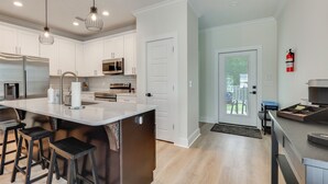 A modern kitchen with white cabinets, stainless steel appliances, a large island with stools, pendant lighting, and a fire extinguisher on the wall. - New! Foley Family Escape w/ Fenced Yard (Foley)