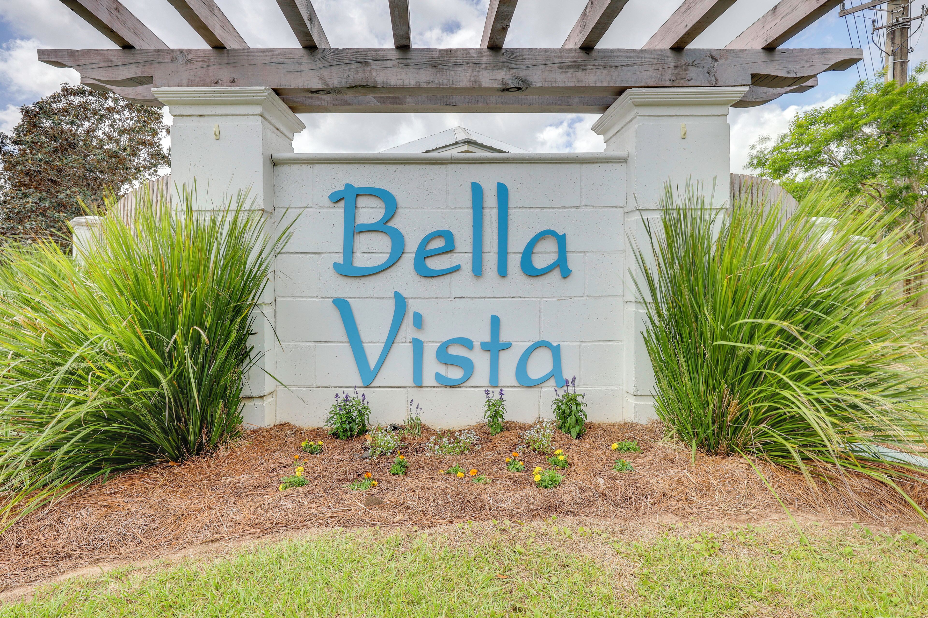 A sign with the name 'Bella Vista' in blue letters, surrounded by green plants and a wooden pergola.