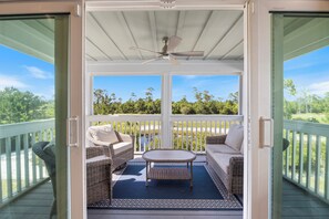 A covered balcony with wicker furniture, a ceiling fan, and a view of greenery. - Introducing Shells N Sea Beach Villa at Lost Key Golf & Beach Club! 4BR 4BA (Pensacola)