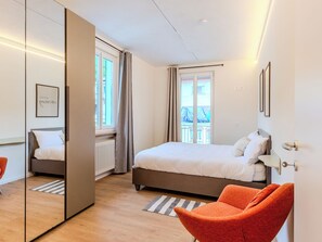 A modern hotel room with a large bed, a sitting area with an orange chair, a large window with curtains, and a view of the outside. - Terrazza Segreta around Como Lake by Interhome (Carlazzo)