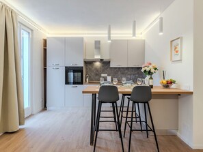 Eine moderne Küche mit weißen Schränken, einem eingebauten Backofen und einer Essecke mit zwei schwarzen Barhocker.