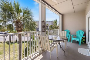 En balkon med bord og stole, palmer og udsigt til en bygning i baggrunden.