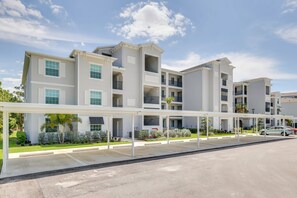 A multi-story residential building with balconies, a covered parking area, and a clear sky. - Golf + Poolside Fun! Extended Base in Ibis Landing (Lehigh Acres)