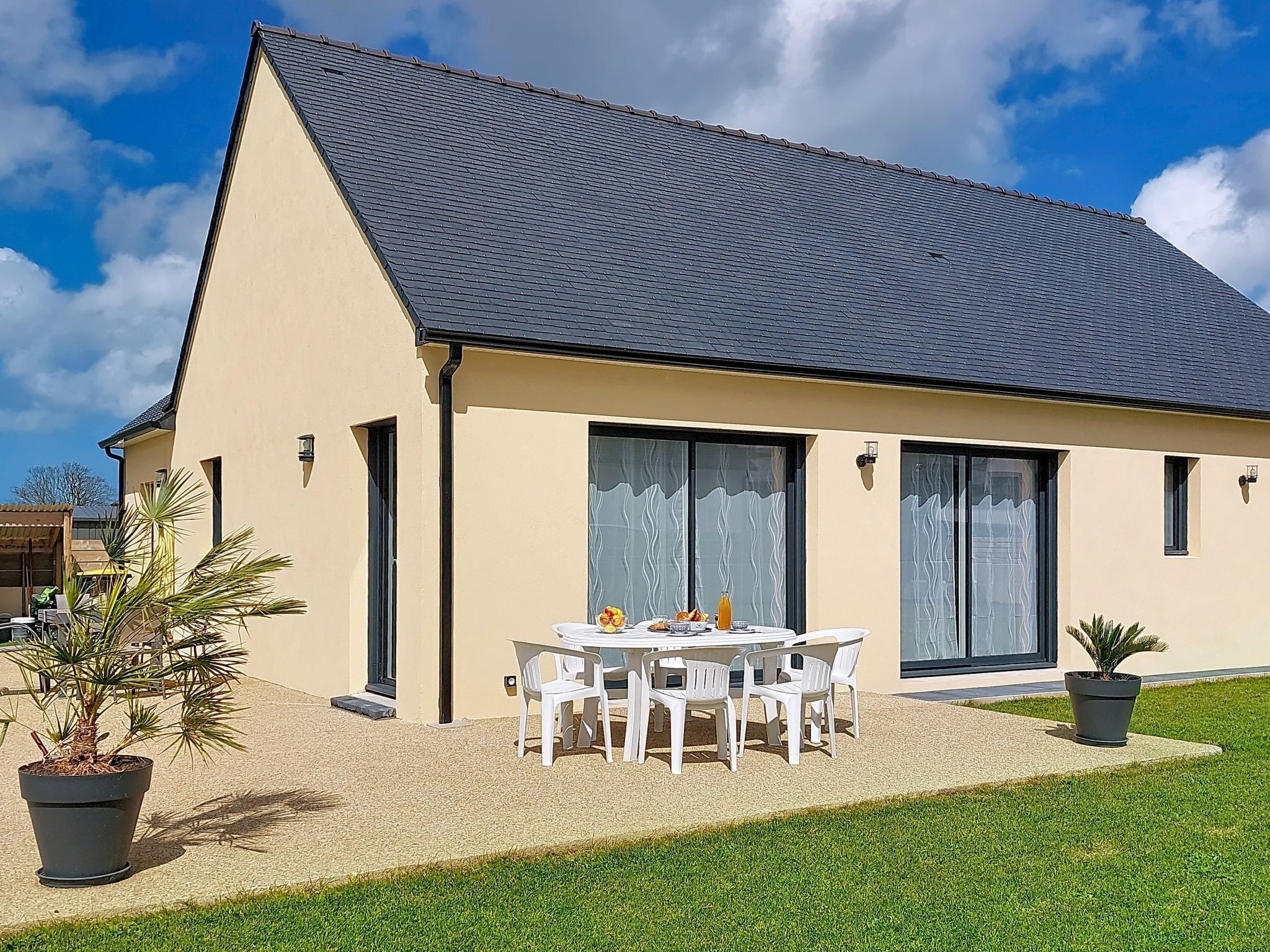 A single-story house with a dark roof, large windows, and a patio with a table and chairs.