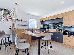 Eine moderne Küche mit Holzschränken, einer zentralen Kochinsel mit Hockern und einem großen Fenster.