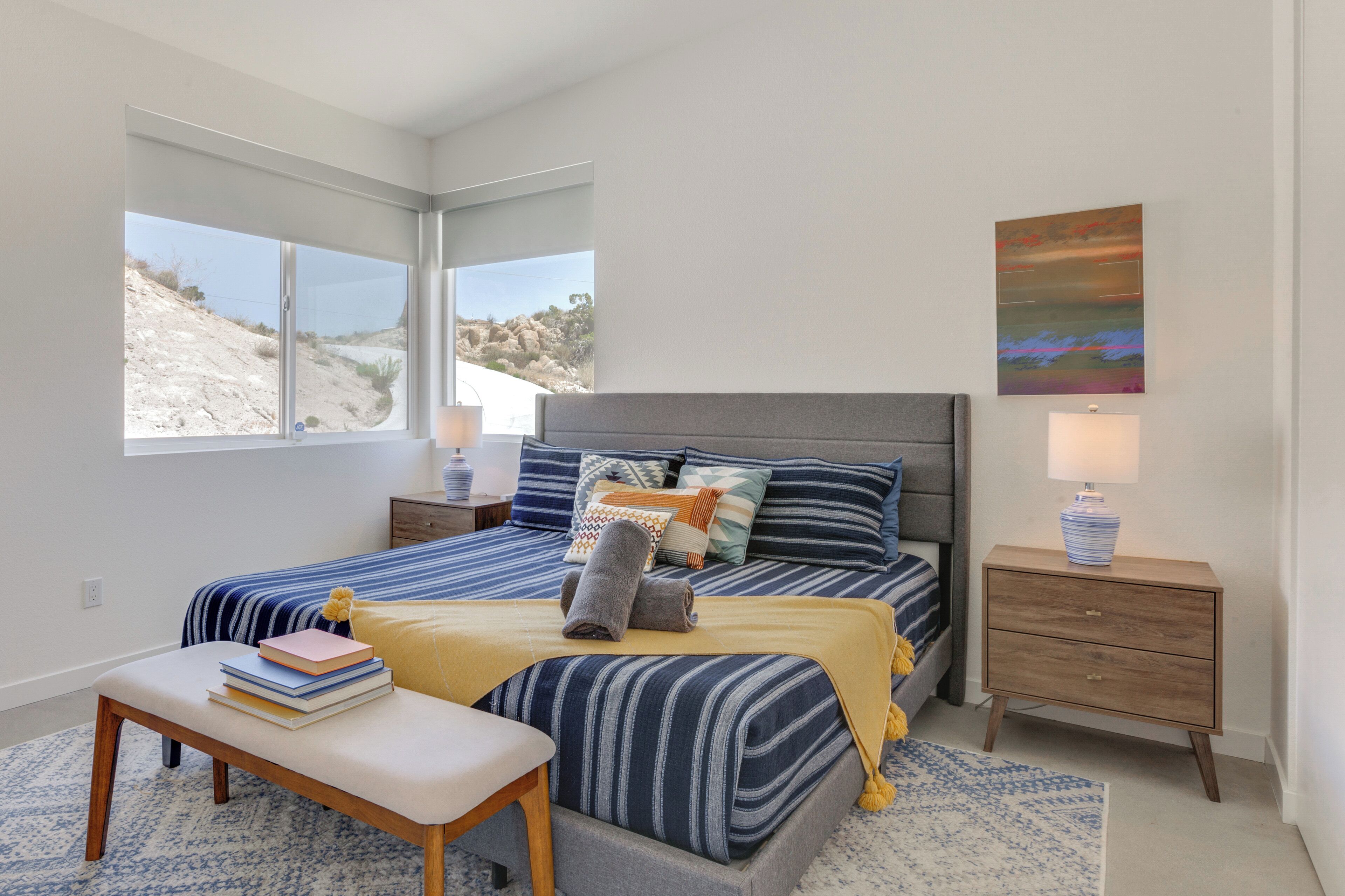 Un dormitorio con cama, mesitas de noche, un banco y ventana con vista a un paisaje rocoso.