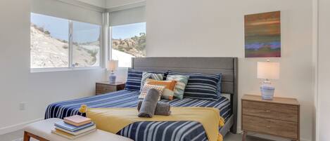 Un dormitorio con cama, mesitas de noche, un banco y ventana con vista a un paisaje rocoso.