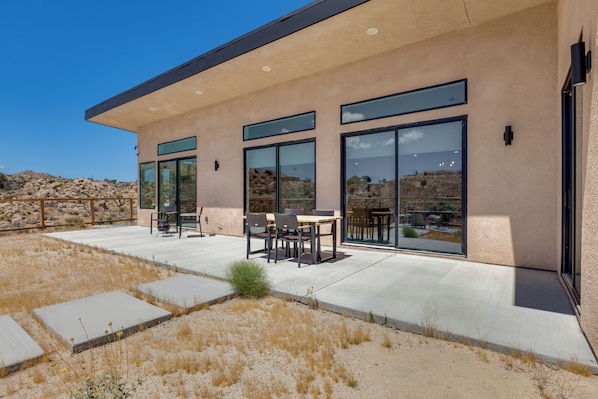 A modern building with large windows, a patio area with outdoor furniture, and a view of the surrounding landscape.