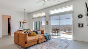 A spacious living room with a large sectional sofa, a chandelier, and a view of the outdoors through large sliding glass doors. - Hot Tub & Views! Contemporary Yucca Valley Retreat (Yucca Valley)
